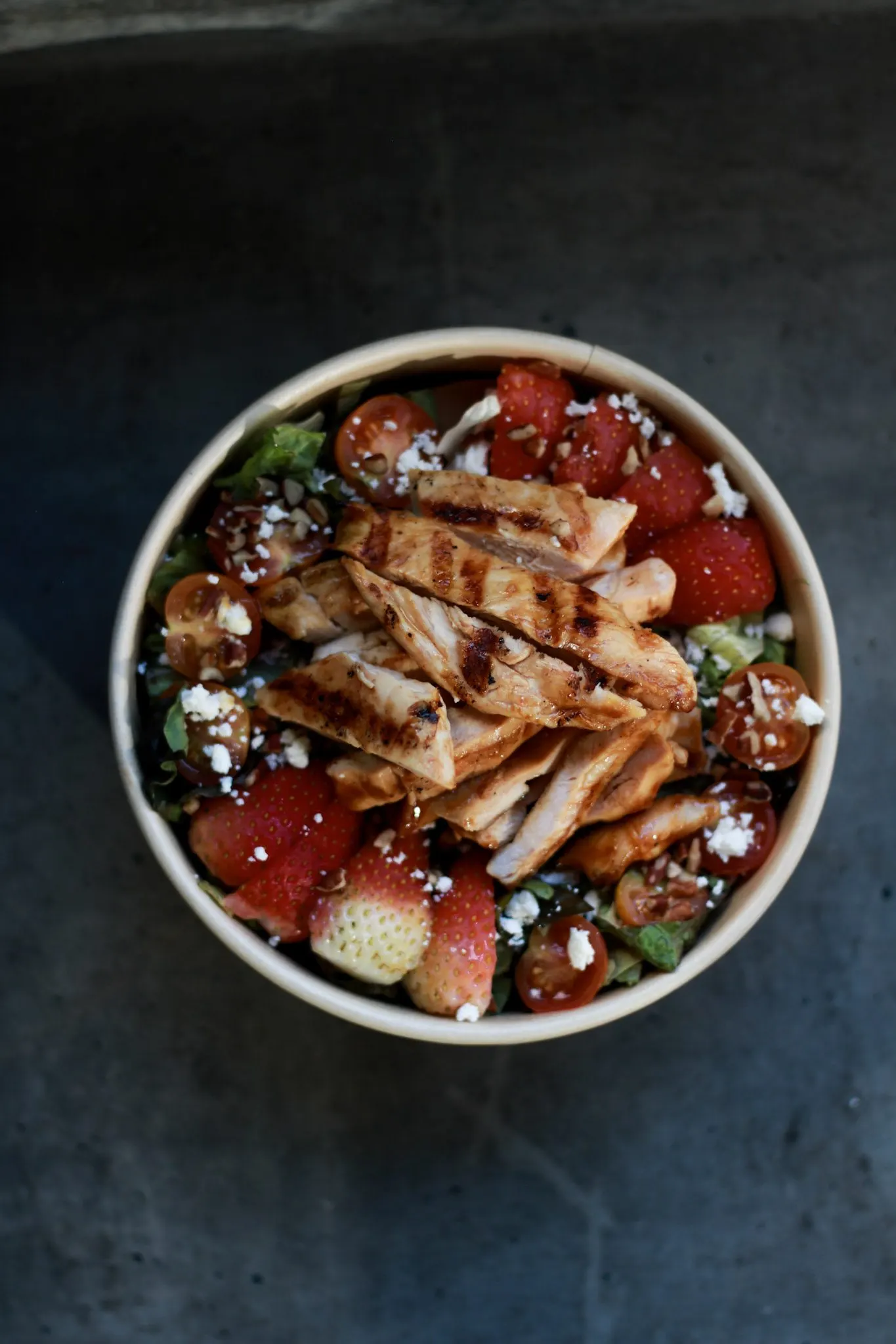 Fresh salad vista desde arriba sobre concreto oscuro: pollo al grill, fresas, tomate cherry y queso feta